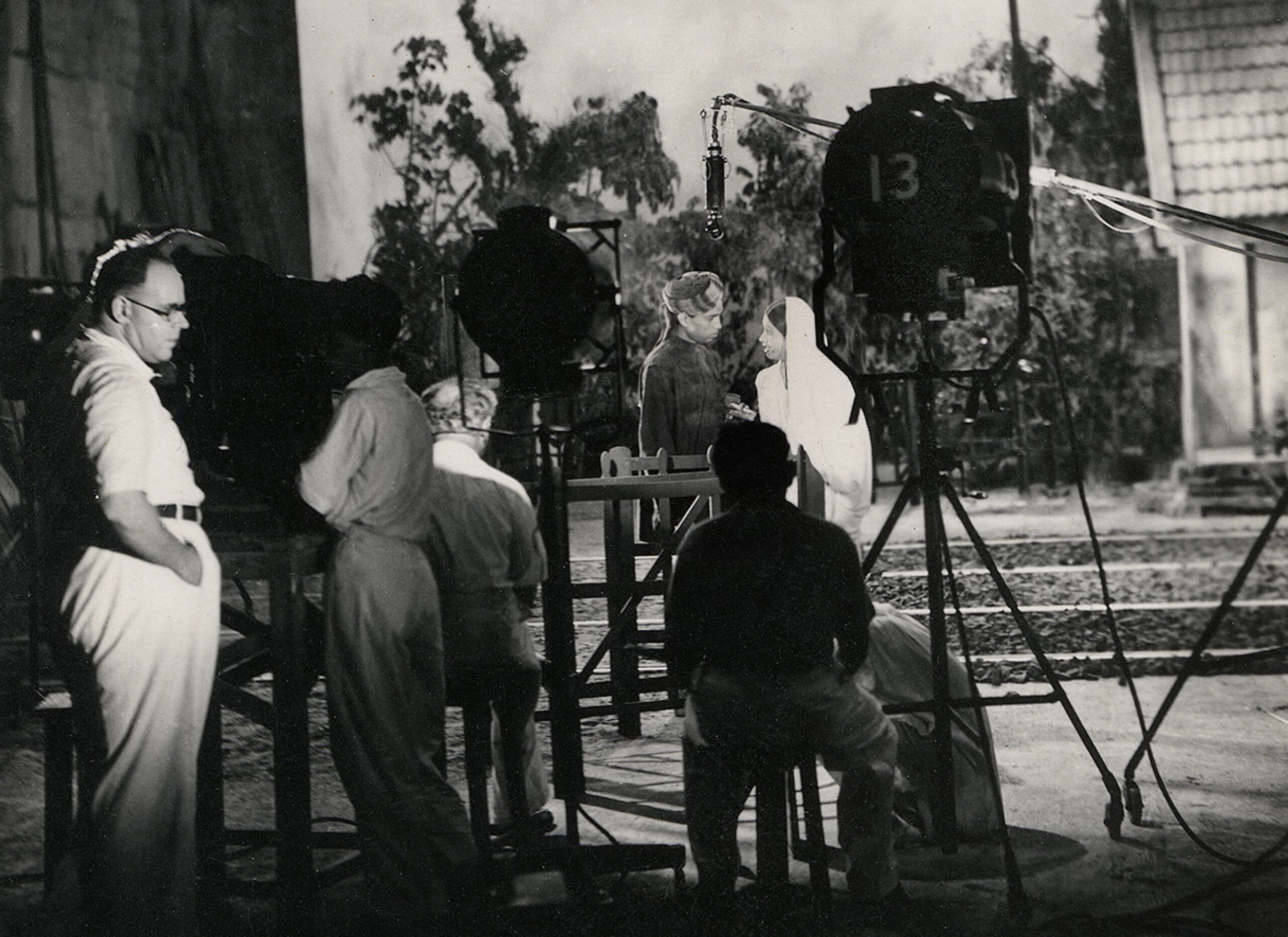 black and white photograph from a film set showing four crew members and two actors with various filming equipment