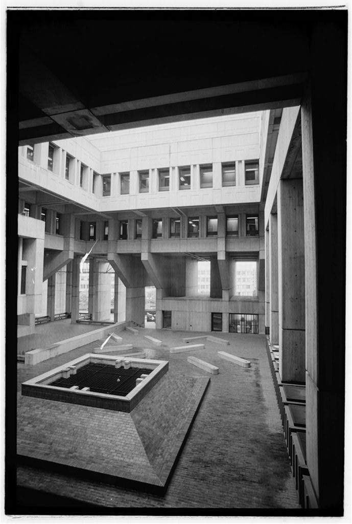 The black and white photograph shows an interior courtyard of the building, a large concrete structure with many windows,